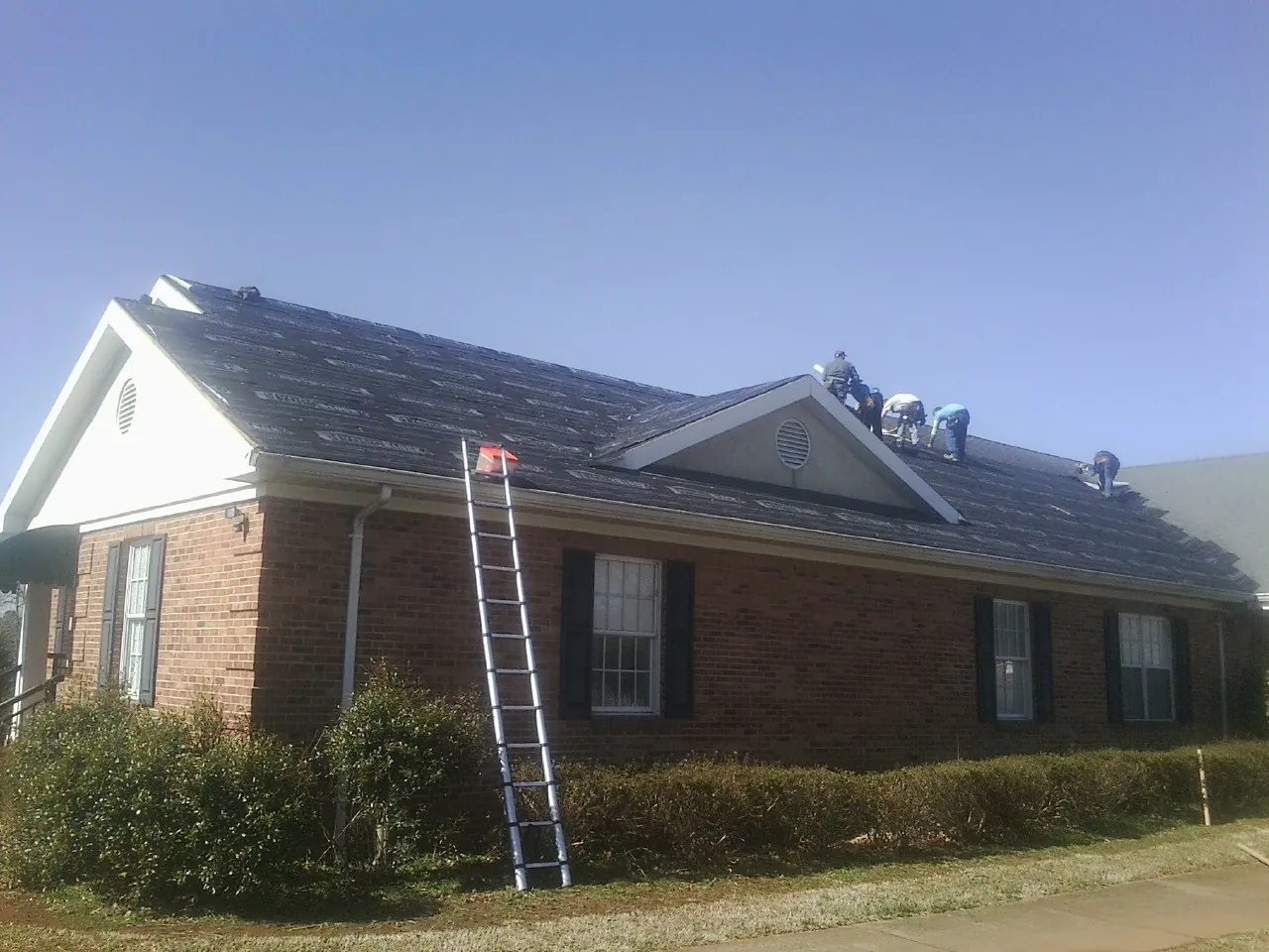 Crew tearing shingles off a brick ranch roof with a ladder set — Emergency Roof Repair work by our crew in Timber