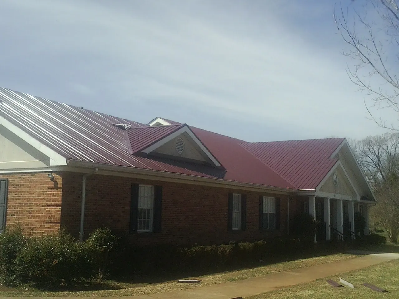 Red metal roof with gabled entries on a long brick building, from a Hail Damage Roof Repair job in Timber