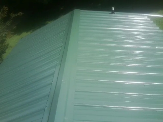 New green metal panels meeting at the ridge of a roof — Flat Roof Repair work by our crew in Timber