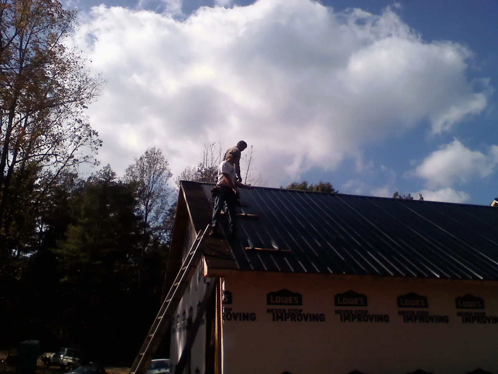 Roofer fastening dark metal panels high against a cloudy sky, from a Roof Inspection job in Timber